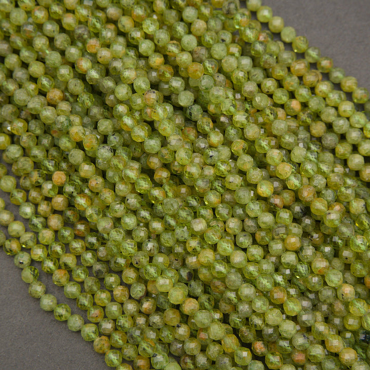 Faceted round beads in a translucent olive green color with subtle yellow and orange undertones, arranged in a diagonal pile on a dark gray background.
