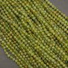 Faceted round beads in a translucent olive green color with subtle yellow and orange undertones, arranged in a diagonal pile on a dark gray background.