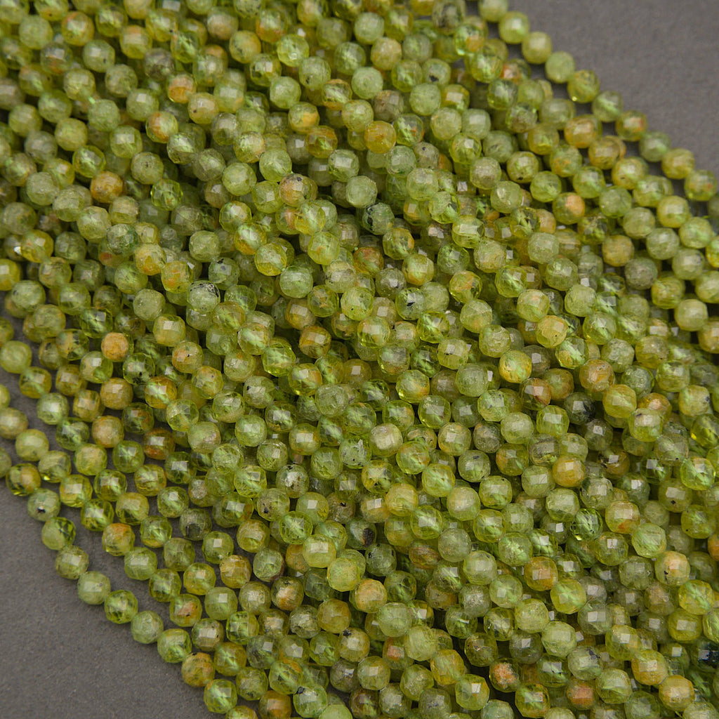 Faceted round beads in a translucent olive green color with subtle yellow and orange undertones, arranged in a diagonal pile on a dark gray background.