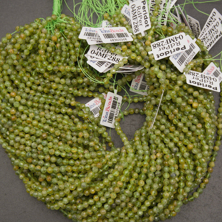 Coiled strands of faceted olive green beads with white product tags attached, photographed on a dark gray surface.