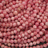 A close-up pile of round, glossy pink beads with white marbled streaks and some warm peachy-brown tones.