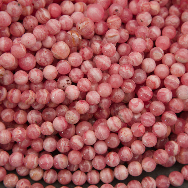 A close-up pile of round, glossy pink beads with white marbled streaks and some warm peachy-brown tones.