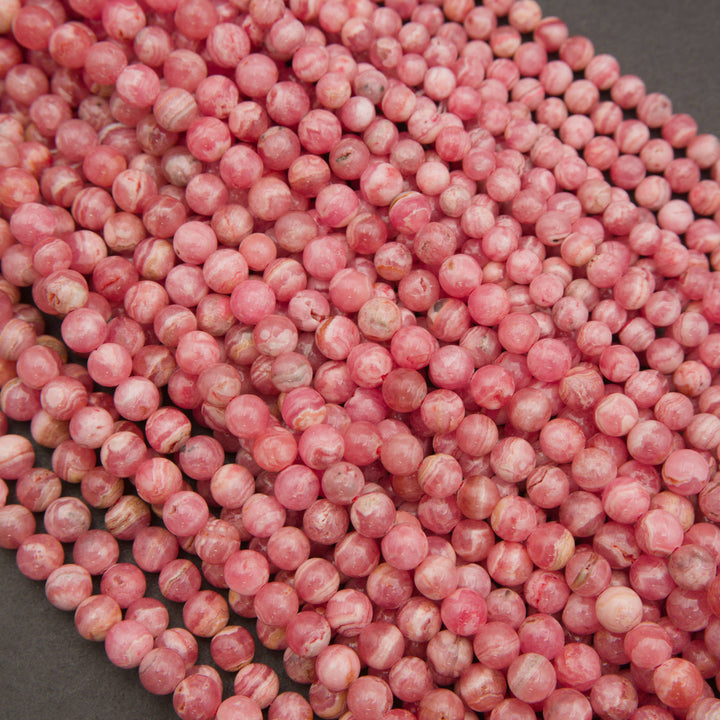 A pile of small round pink beads with white marbled streaks, photographed close-up on a dark gray surface.