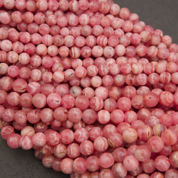 A pile of round, pink marbled beads with white veining, photographed close-up on a dark gray surface.