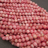 A pile of round, pink marbled beads with white veining, photographed close-up on a dark gray surface.