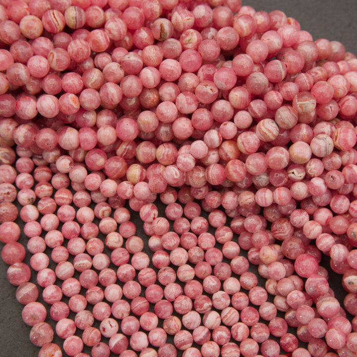 A pile of small round pink beads with white marbled swirls, photographed close-up on a dark gray surface.