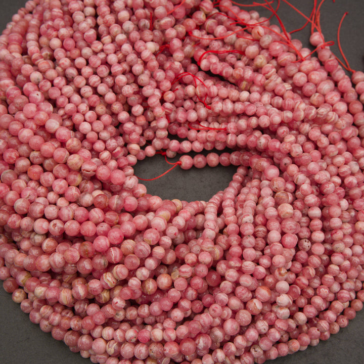 Coiled strands of round pink marbled beads with red thread ties, photographed on a dark gray surface.