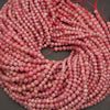 Coiled strands of round pink marbled beads with red thread ties, photographed on a dark gray surface.