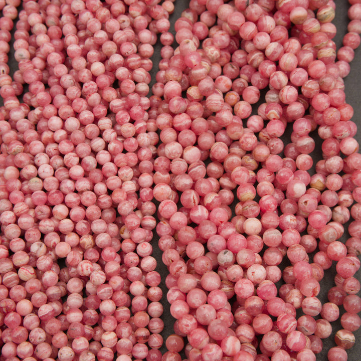A close-up of many small round beads in a dusty pink color with white marbling, arranged in vertical strands.