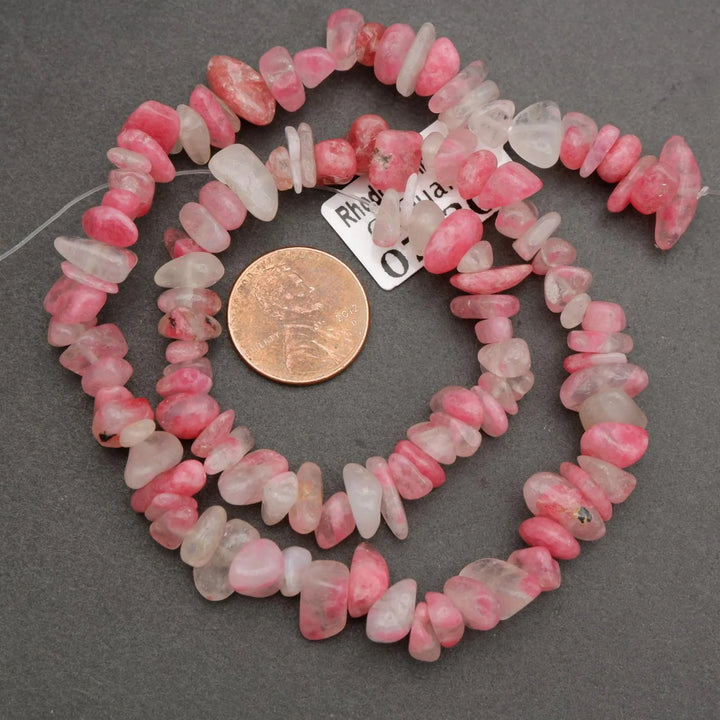 Necklace of pink and white beads with a coin for scale on a gray background