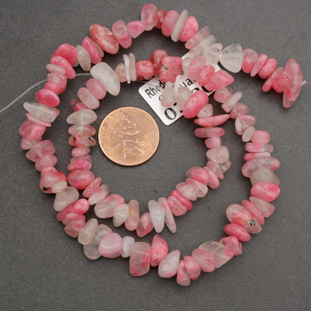 Necklace of pink and white beads with a coin for scale on a gray background