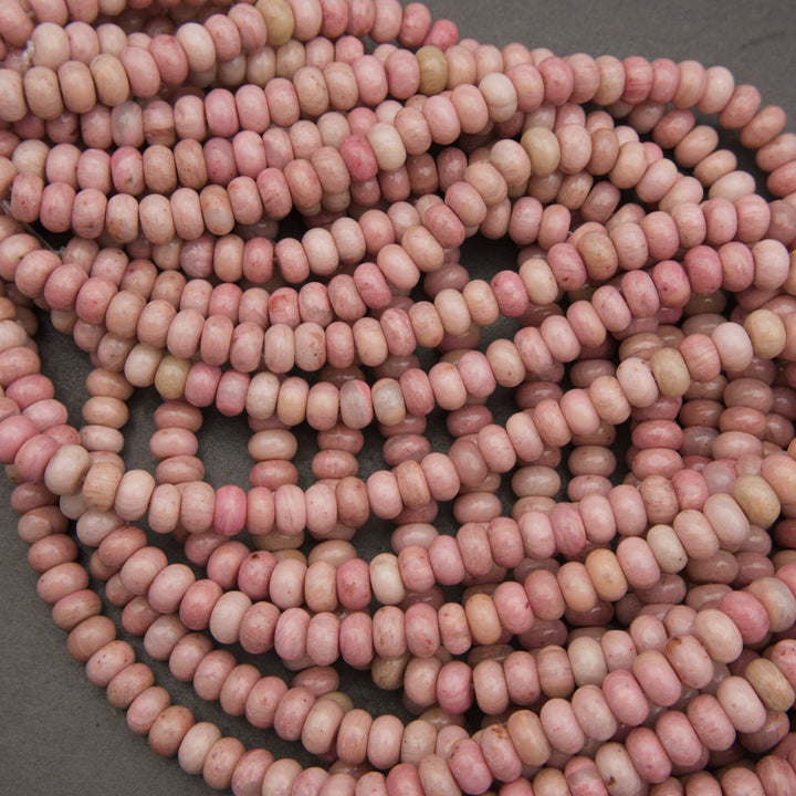 A pile of small, elongated oval beads in a marbled pink and cream color, arranged on a dark gray surface.