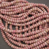 A pile of small, elongated oval beads in a marbled pink and cream color, arranged on a dark gray surface.