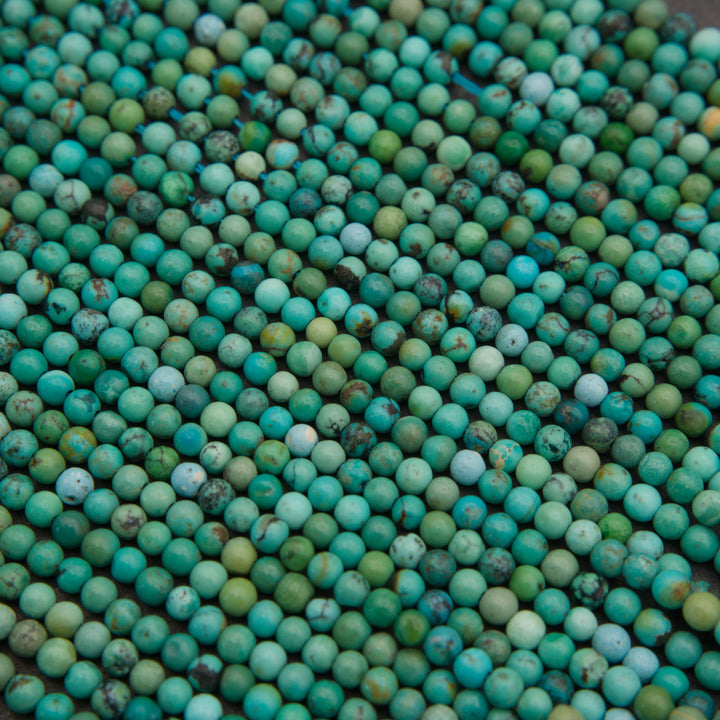 Small turquoise round beads in mixed shades of blue and green with rustic brown inclusions and a smooth finish.