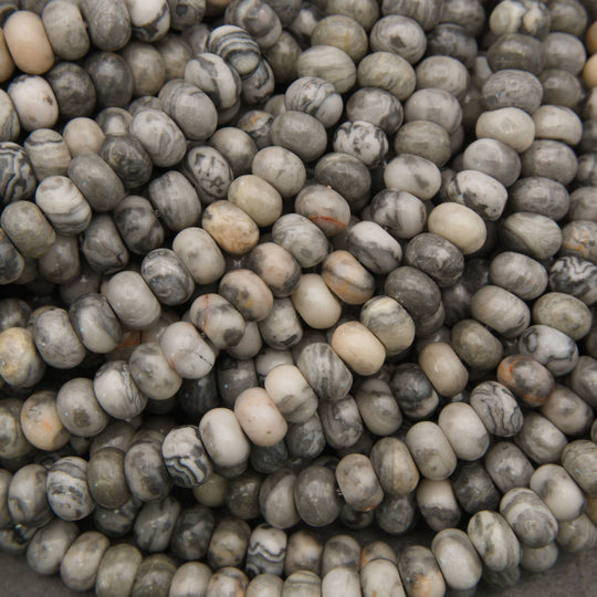 A close-up pile of oval stone beads in a marbled pattern of gray, white, beige, and black.