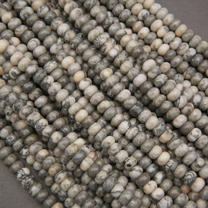Close-up of multiple strands of round stone beads in a marbled mix of gray, beige, cream, and black, arranged diagonally.
