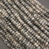 Close-up of multiple strands of round stone beads in a marbled mix of gray, beige, cream, and black, arranged diagonally.