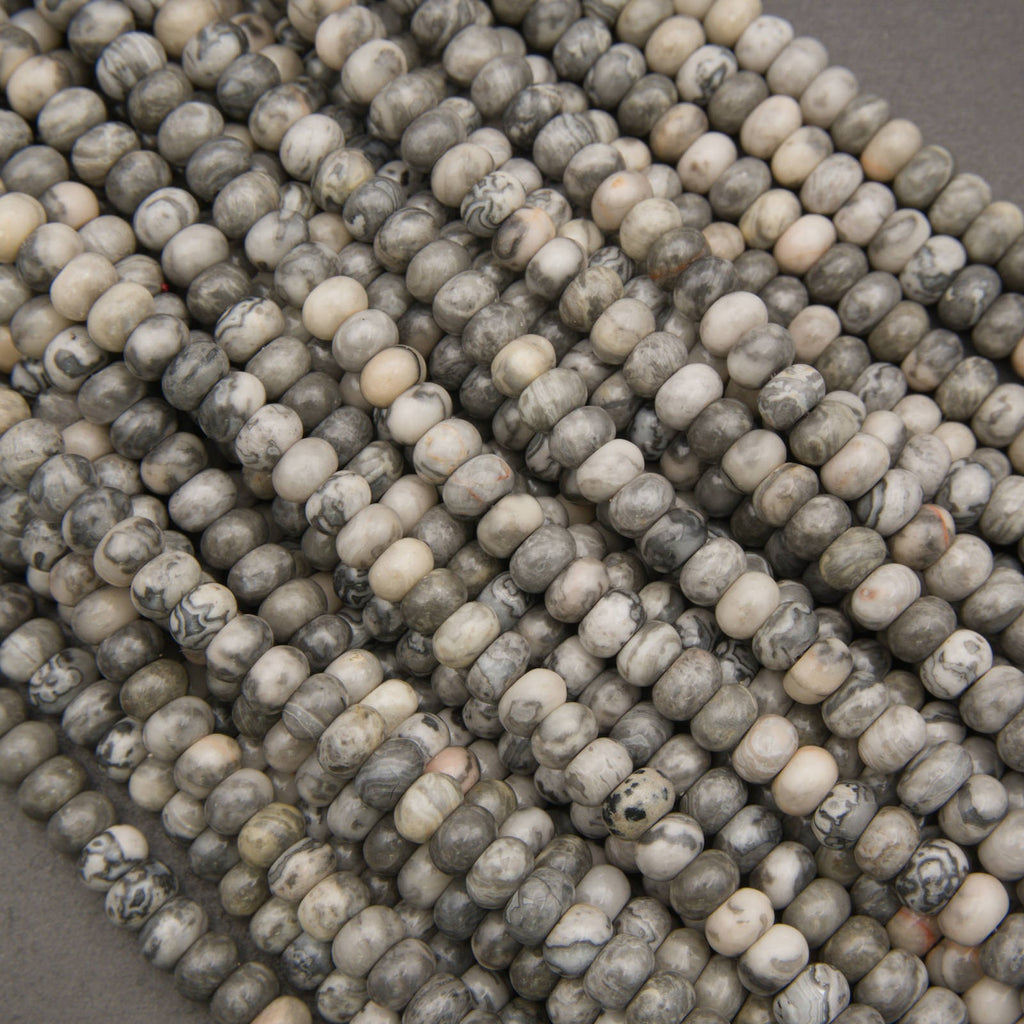 Close-up of multiple strands of round stone beads in a marbled mix of gray, beige, cream, and black, arranged diagonally.