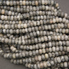 Close-up of multiple strands of small cylindrical beads with a marbled pattern in gray, white, and black, arranged on a neutral gray surface.