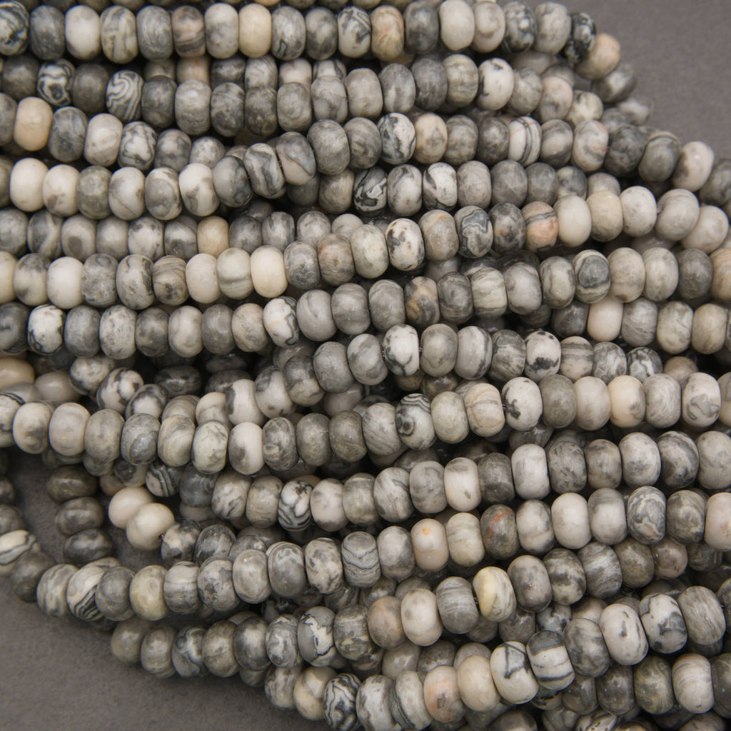 Close-up of multiple strands of small cylindrical beads with a marbled pattern in gray, white, and black, arranged on a neutral gray surface.