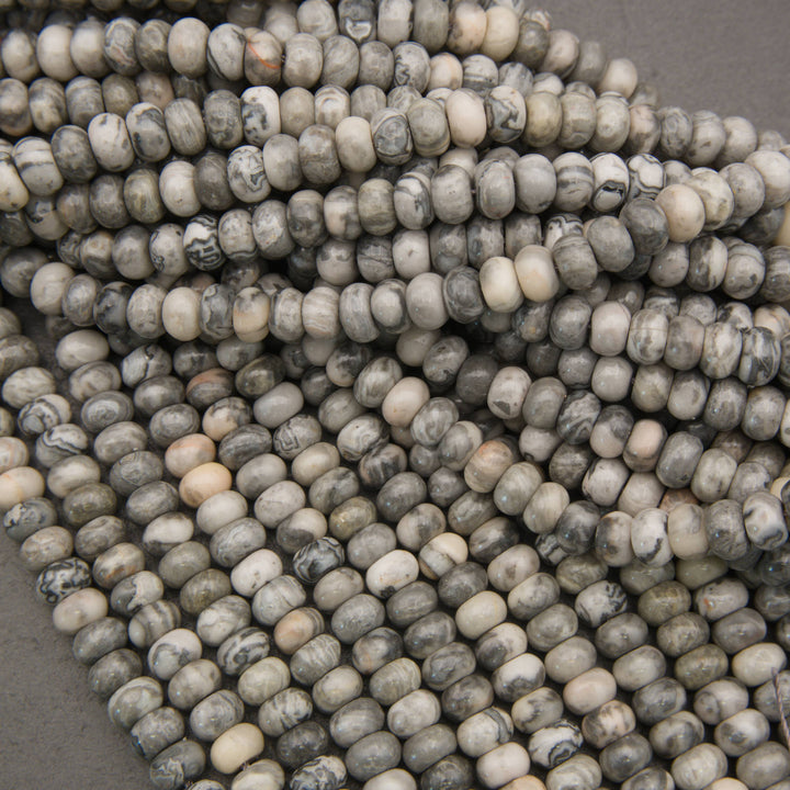 A close-up of many small oval beads in a marbled stone pattern, showing gray, white, and black tones, arranged in overlapping strands.