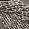 A close-up of many small oval beads in a marbled stone pattern, showing gray, white, and black tones, arranged in overlapping strands.