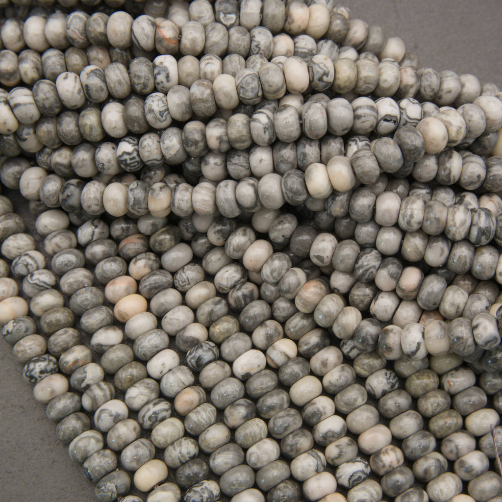 A close-up of many small oval beads in a marbled stone pattern, showing gray, white, and black tones, arranged in overlapping strands.