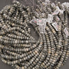 Multiple strands of round stone beads in gray, beige, and white marbled colors, each tied with a white price tag, arranged on a gray surface.