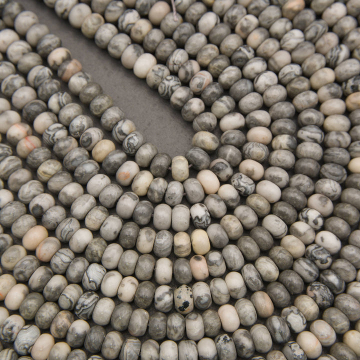 Close-up of multiple strands of small oval beads made from a speckled stone with gray, beige, white, and black marbling.