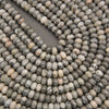 Close-up of multiple strands of small oval beads made from a speckled stone with gray, beige, white, and black marbling.