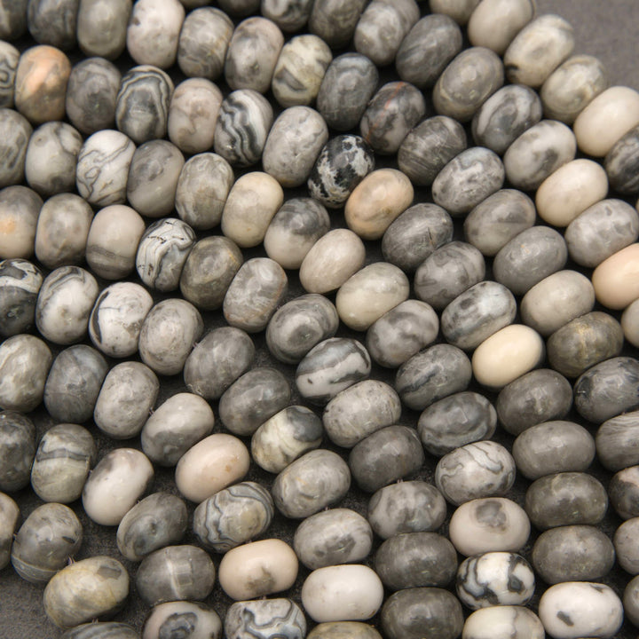 A close-up pile of small polished stone beads or pebbles in mixed gray, beige, white, and black marbled tones.