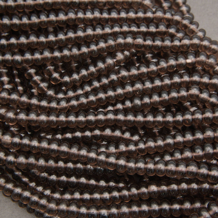 A close-up of multiple strands of small, dark brown translucent glass beads with metallic bronze reflections, coiled together on a neutral gray background.