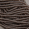 A close-up of multiple strands of small, dark brown translucent glass beads with metallic bronze reflections, coiled together on a neutral gray background.