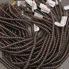 A pile of dark brown translucent gemstone beads with white product tags showing details like 'Ice Obsidian' and 'Cushion Agate'.