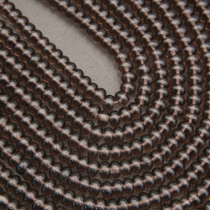A close-up of a coiled strand of small, glossy, dark brown translucent beads on a neutral gray background.