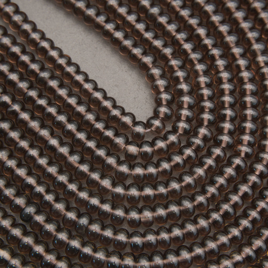 A close-up of a coiled strand of small, glossy, dark brown translucent beads on a neutral gray background.