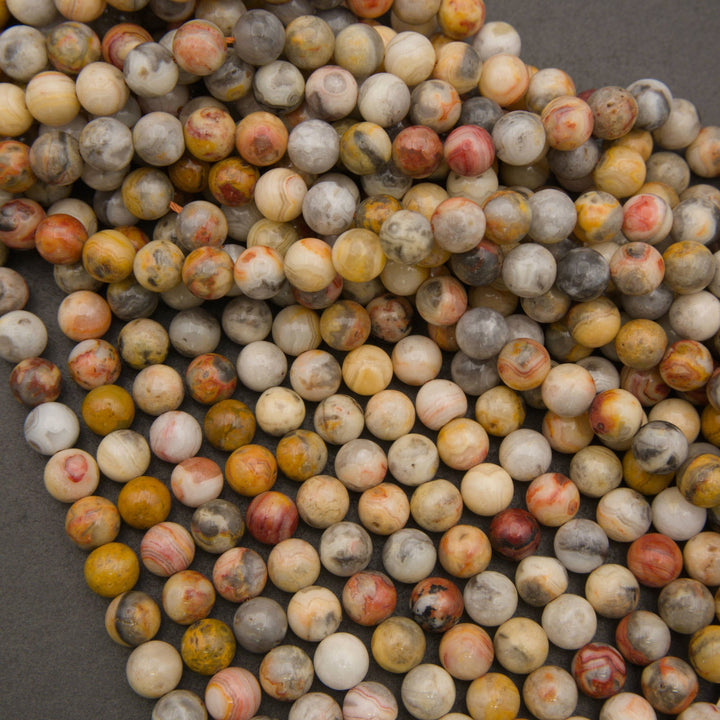 A pile of round, polished gemstone beads in a marbled pattern of yellow, orange, red, gray, and cream on a dark gray background.