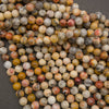 A pile of round, polished gemstone beads in a marbled pattern of yellow, orange, red, gray, and cream on a dark gray background.