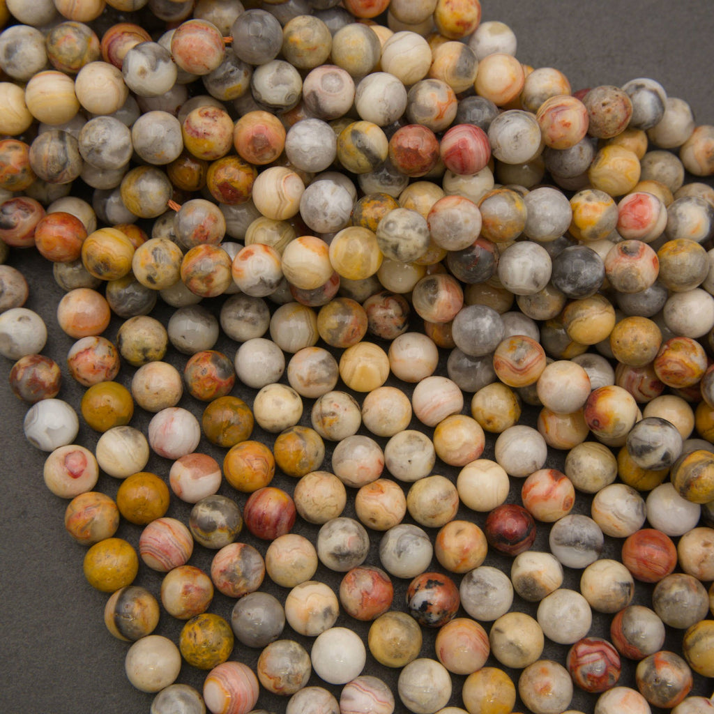 A pile of round, polished gemstone beads in a marbled pattern of yellow, orange, red, gray, and cream on a dark gray background.