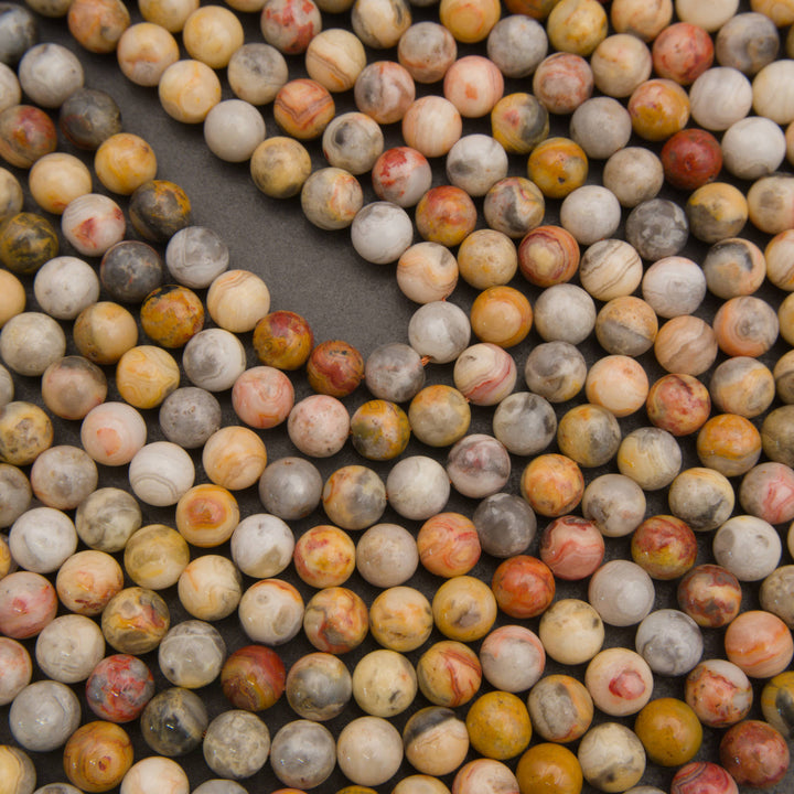 Round gemstone beads in a marbled mix of cream, yellow, orange, red, gray, and brown, arranged in a curved pattern on a dark gray background.