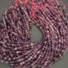 Close-up of a coiled string of beads with pink and purple threads on a gray background