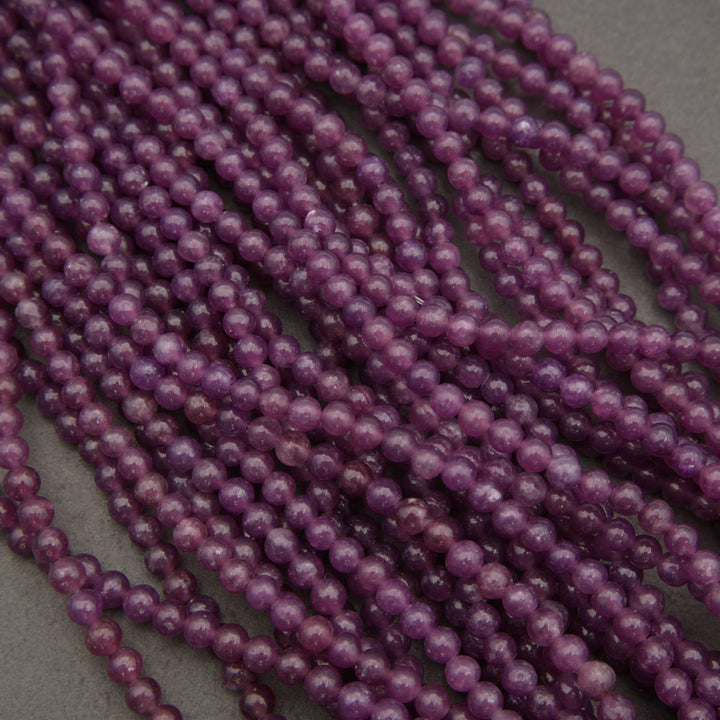 Multiple strands of small, polished purple beads arranged in parallel rows on a neutral gray background.