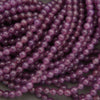 Purple translucent round beads strung in multiple strands, photographed close-up on a neutral gray surface.