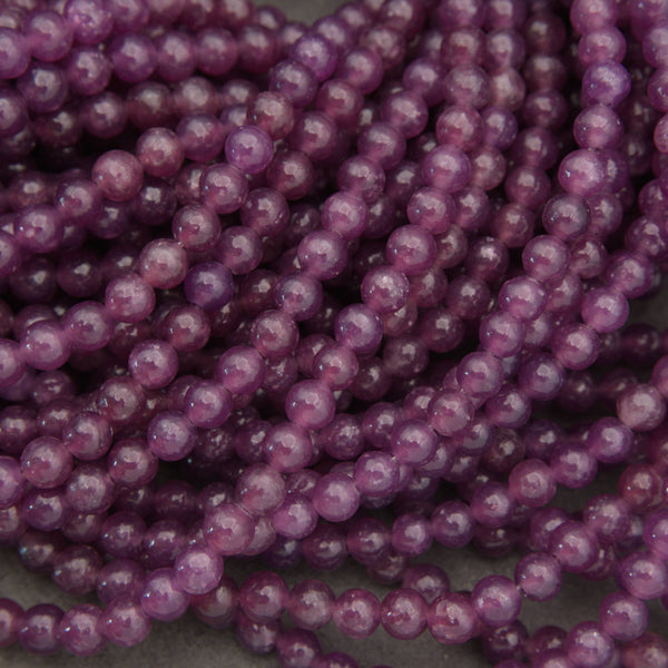 Purple translucent round beads strung in multiple strands, photographed close-up on a neutral gray surface.