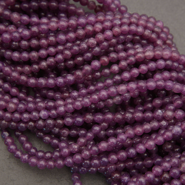 Purple translucent round beads strung in multiple strands, photographed close-up on a neutral gray surface.