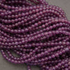Purple translucent round beads strung in multiple strands, photographed close-up on a neutral gray surface.