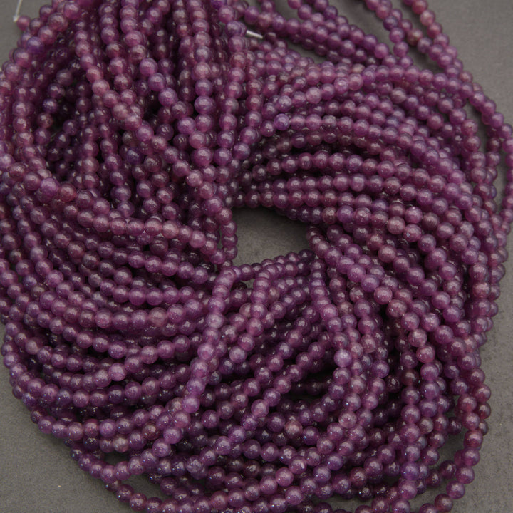 Purple translucent round beads strung in multiple strands, photographed close-up on a neutral gray surface.