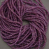 Purple translucent round beads strung in multiple strands, photographed close-up on a neutral gray surface.