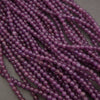 Multiple strands of small, polished purple beads arranged in parallel rows on a neutral gray background.