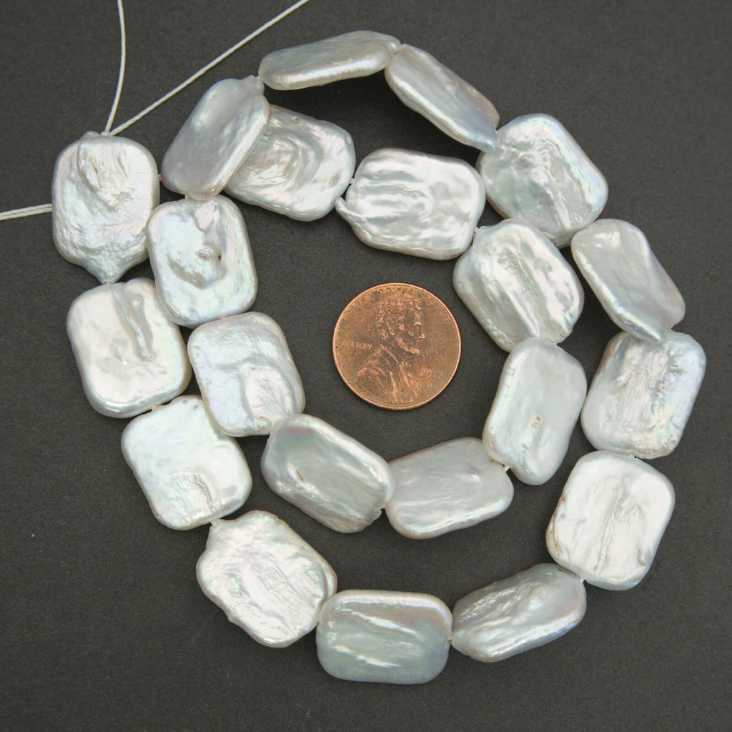 String of white baroque pearl beads with a penny for size comparison on a dark background